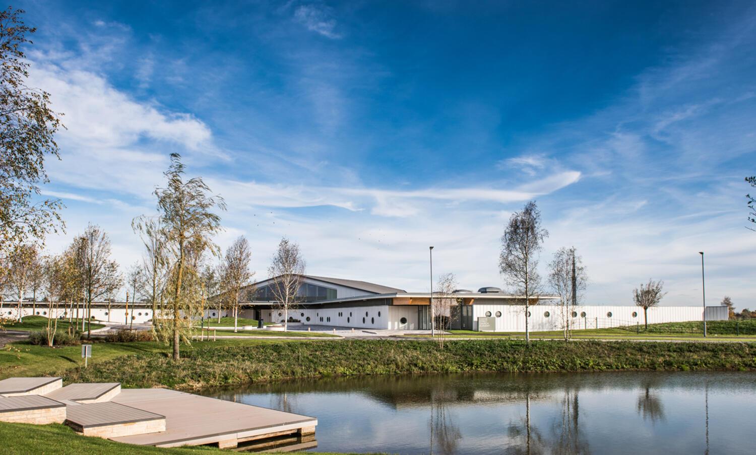 A new one story school building with circular windows and glass apex roof with trees set on a grassy bank.  