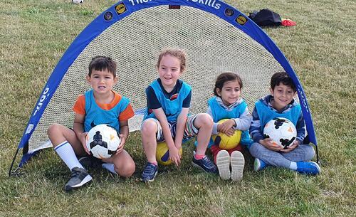 Four children sitting holding footballs learning football skills