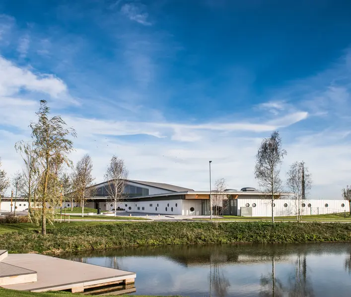 A new one story school building with circular windows and glass apex roof with trees set on a grassy bank.  